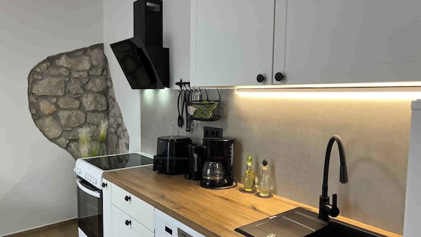 Une cuisine moderne avec des armoires blanches, un mur d’accent en pierre, une cuisinière encastrée, une machine à café, une bouilloire et un évier avec un robinet.