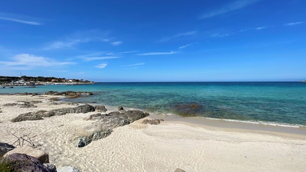 A beach with clear turquoise water, rocky shoreline, and a distant town. - Beachfront villa with pool (Lumio)