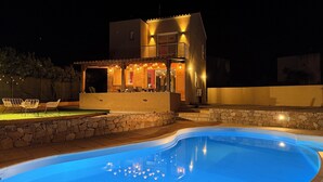 A modern outdoor pool area with a stone wall and a poolside seating area. - Beachfront villa with pool (Lumio)