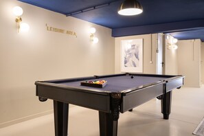 A pool table with balls in the center, a wall with 'LEISURE AREA' text, and a framed picture on the wall.