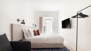 A bedroom with a bed, a sofa, a TV, a floor lamp, and a window with blinds. - Lapa Diplomatic Flat 0 4 by Feel Lisboa (Lisbon)