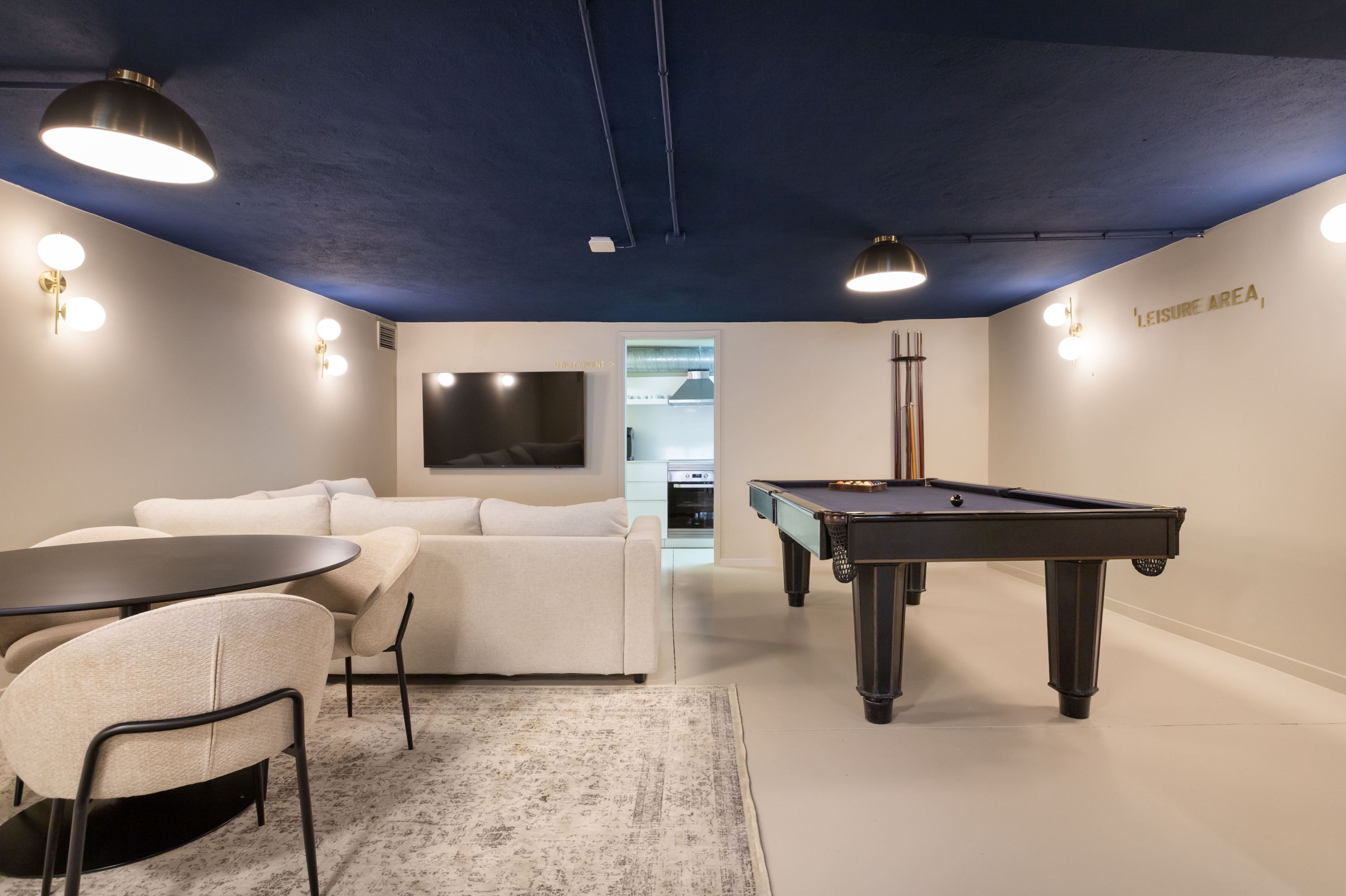 Een moderne kamer met een pooltafel, een bank, een televisie en een kitchenette.