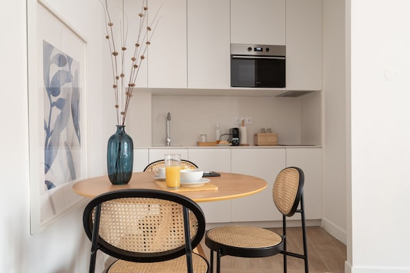 Una cocina moderna con armarios blancos, horno integrado y un comedor con mesa redonda y sillas de mimbre.