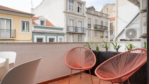 Een balkon met twee rieten stoelen, een witte tafel en potplanten.