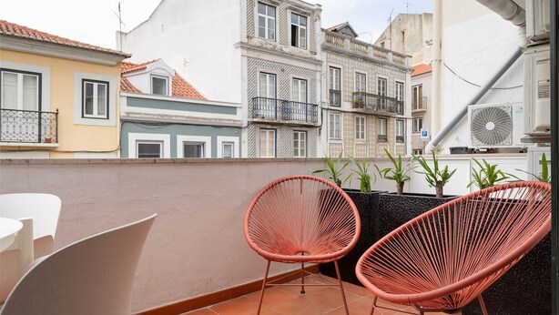 A balcony with two wicker chairs, a white table, and potted plants.