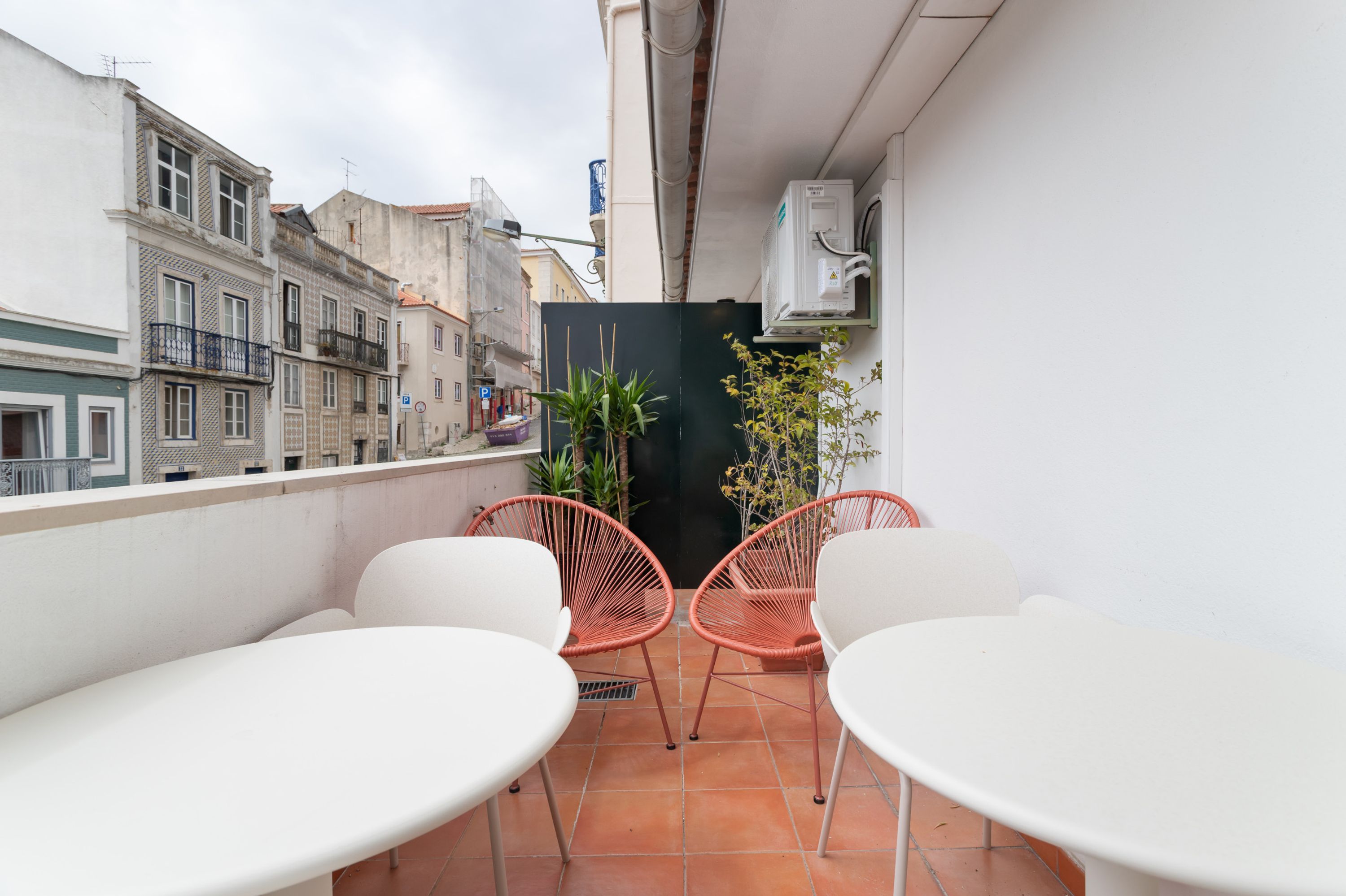 A balcony with white chairs and a table, a potted plant, and a view of buildings.