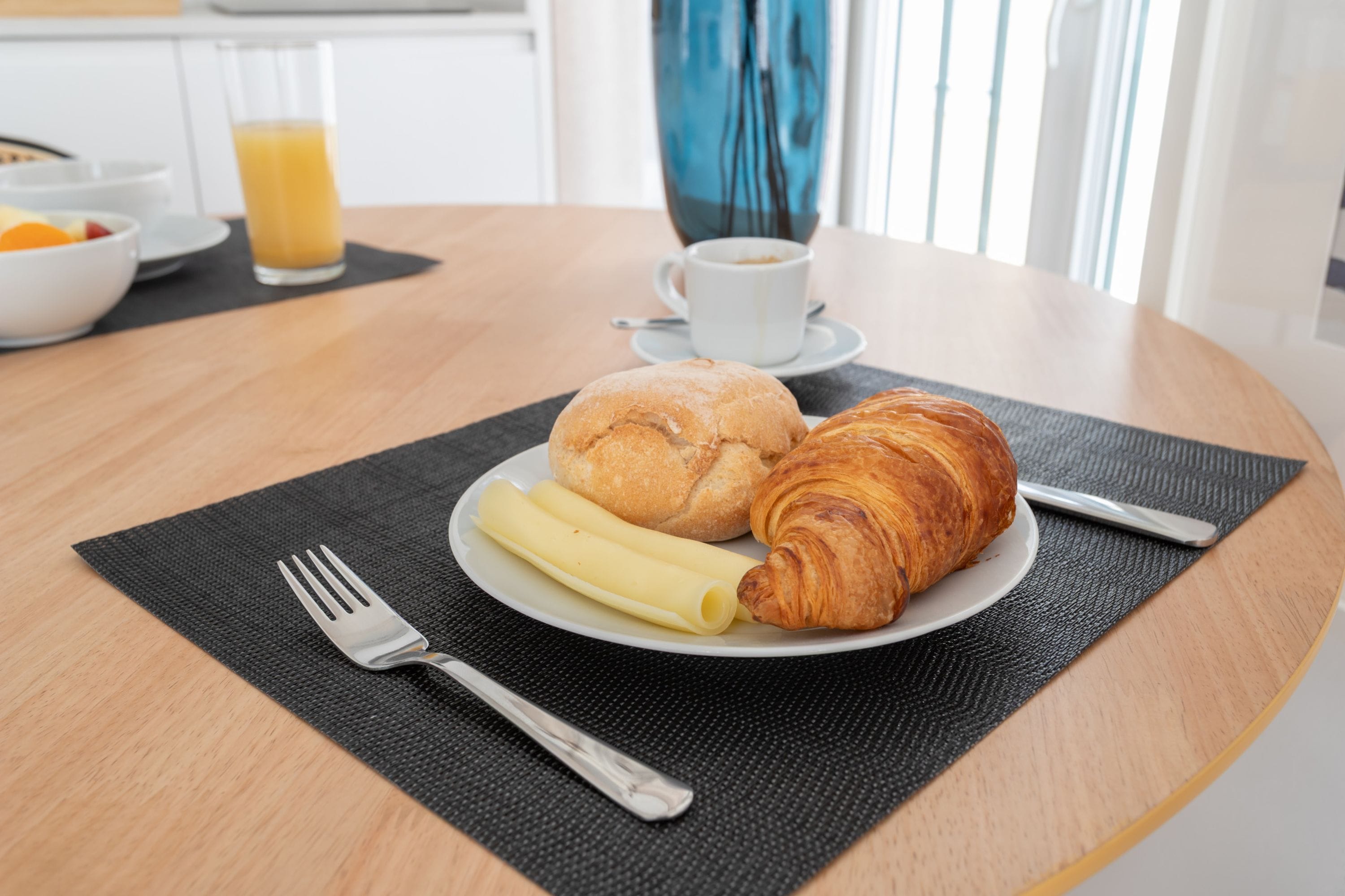 A breakfast setting with croissants, a croissant, and a plate of sliced bananas on a table.