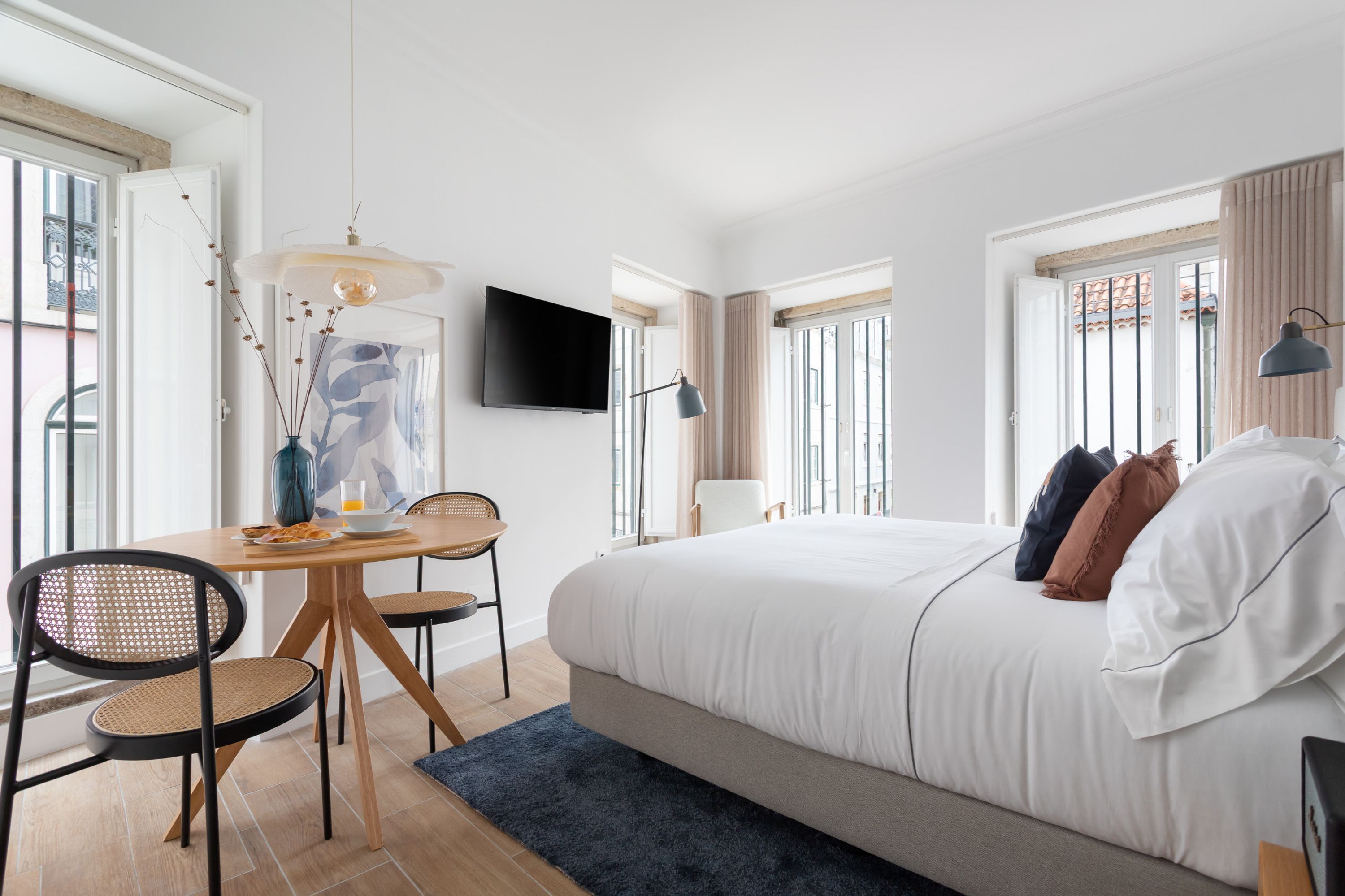 Une chambre à coucher avec un lit, un bureau avec des chaises, une télévision et de grandes fenêtres.