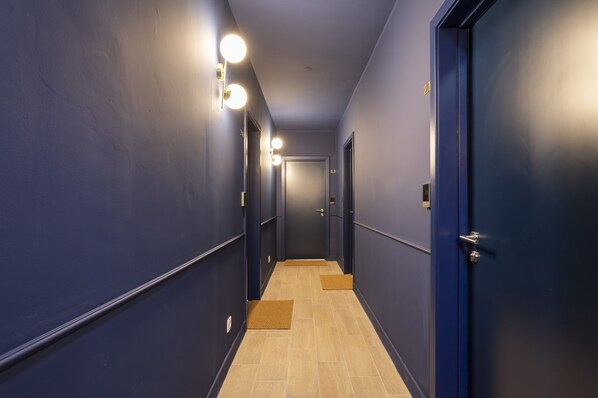 Un pasillo estrecho con paredes azules, suelo de madera y puertas a ambos lados.