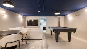 Ein modernes Zimmer mit Billardtisch, einer Couch, einem Fernseher und einer Küchenzeile.