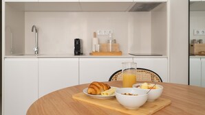 Una cucina moderna con mobili bianchi, un forno a microonde, una macchina da caffè e prodotti per la colazione sul bancone.