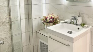 A modern bathroom with a glass shower enclosure, a white sink with a mirror above it, and a decorative flower arrangement on the sink. - Rustic Cottage (Sibiu)