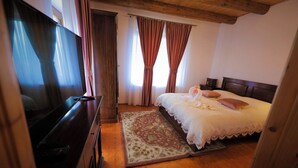 A bedroom with a wooden ceiling, a bed with a white bedspread and pillows, a TV on a wooden cabinet, and a patterned rug. - Rustic Cottage (Sibiu)