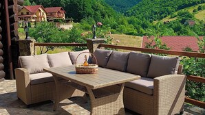 A wicker sofa set with a table, a stone lantern, and a basket on a patio with a mountain view. - Rustic Cottage (Sibiu)