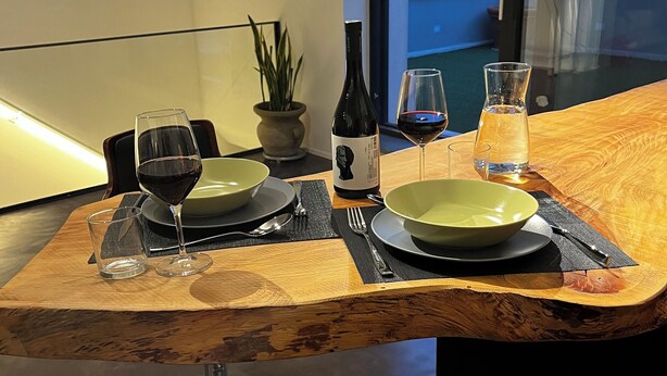 A dining table set with plates, glasses, and a bottle of wine, with a view of the outside through a glass door.