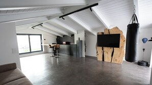 A spacious living area with a large window, a wooden accent wall, a punching bag, and a modern kitchen in the background.
