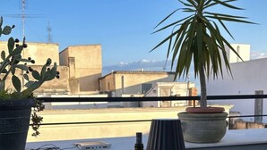 A rooftop terrace with a table set for a meal, including plates of food, glasses of wine, and a bottle of wine.