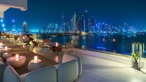 A rooftop bar with modern seating and a view of a city skyline at night. - Spacious Beachside 2BR M at Five Palm Jumeirah (Dubai)