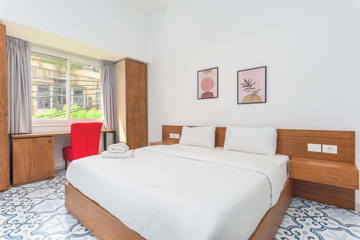 A hotel room with a bed, a desk, a chair, and a window with curtains.