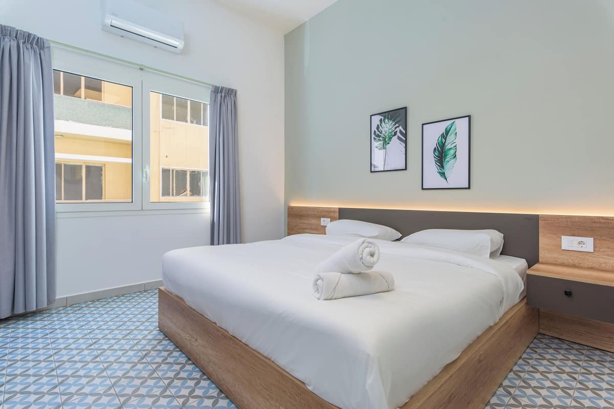 A neatly made bed with a rolled towel, a wooden headboard, and two framed leaf artworks on the wall.