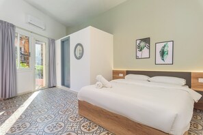 Camera d'albergo con un letto grande, una porta che dà su un balcone e due opere d'arte con foglie incorniciate al muro.
