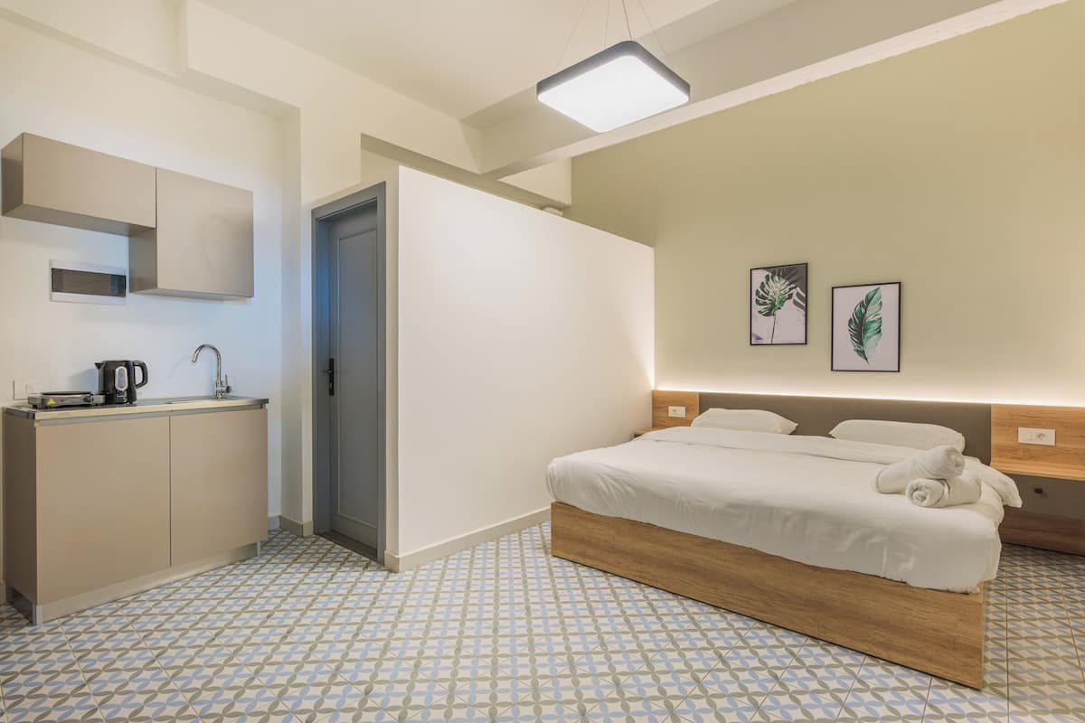 A modern hotel room with a bed, bedside table, and a small kitchenette.