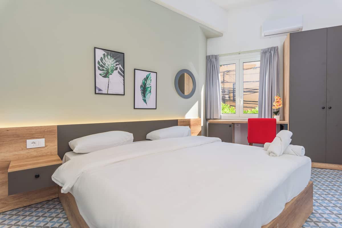 A hotel room with a bed, a desk, a chair, and artwork on the wall.