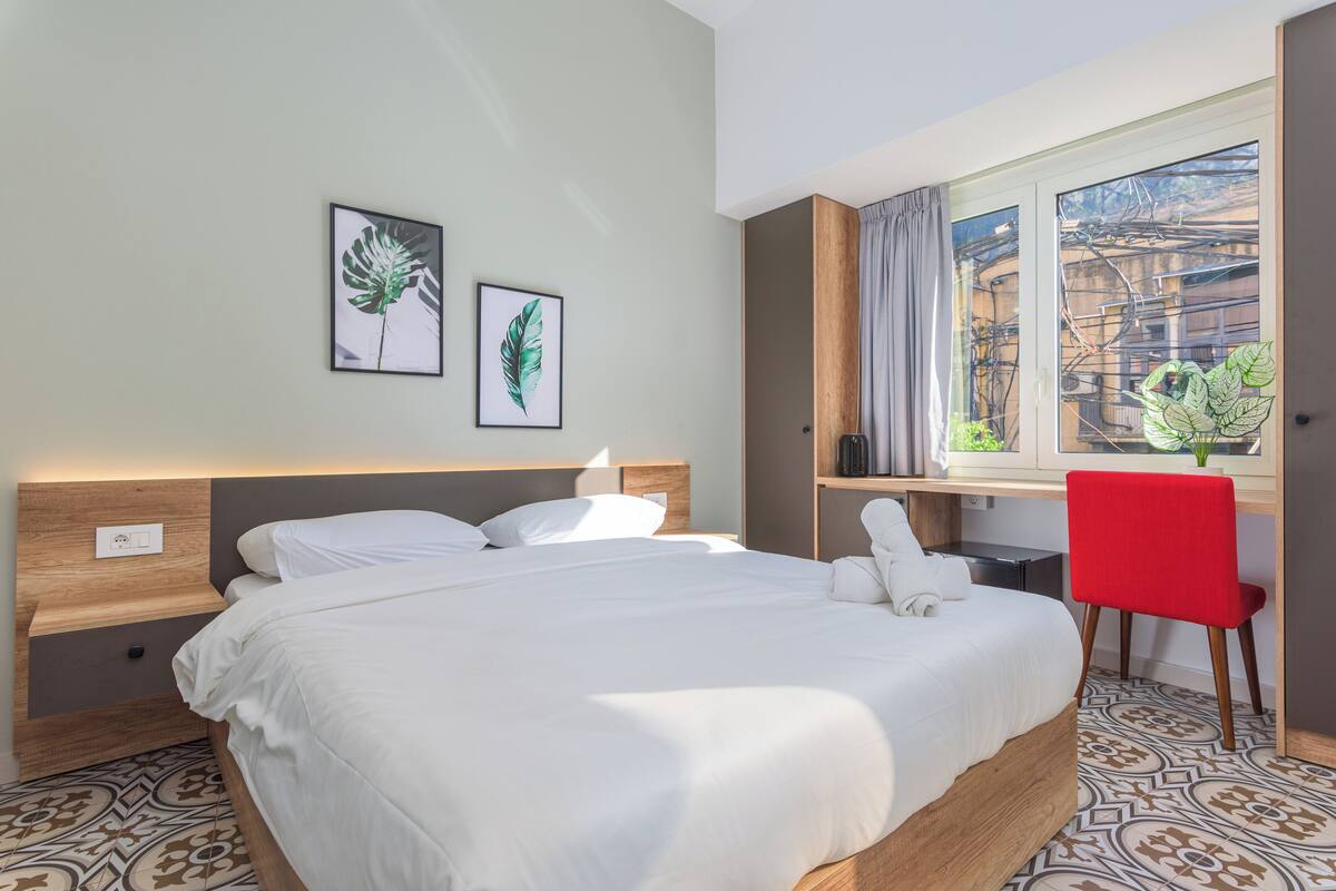 A hotel room with a large bed, a desk, and a window with a view of the city.