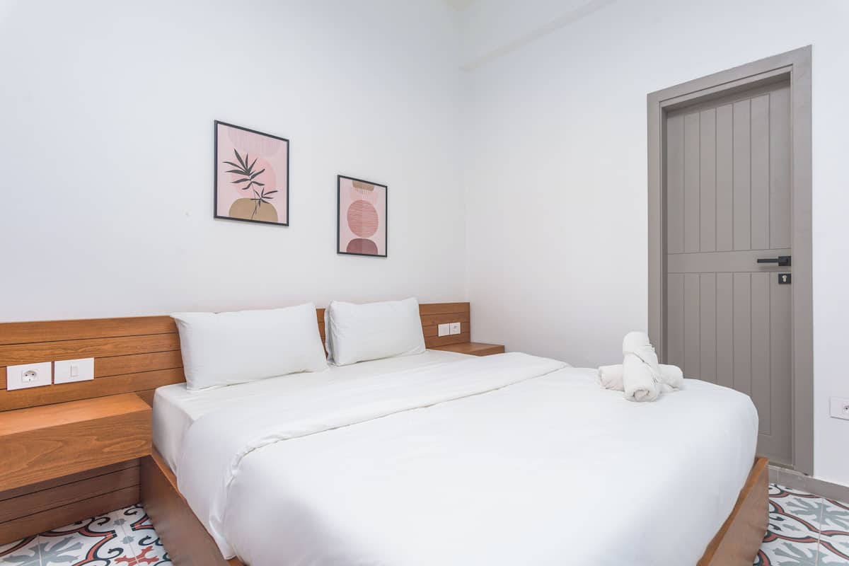 A neatly made bed with white linens, a wooden headboard, and two framed artworks on the wall.
