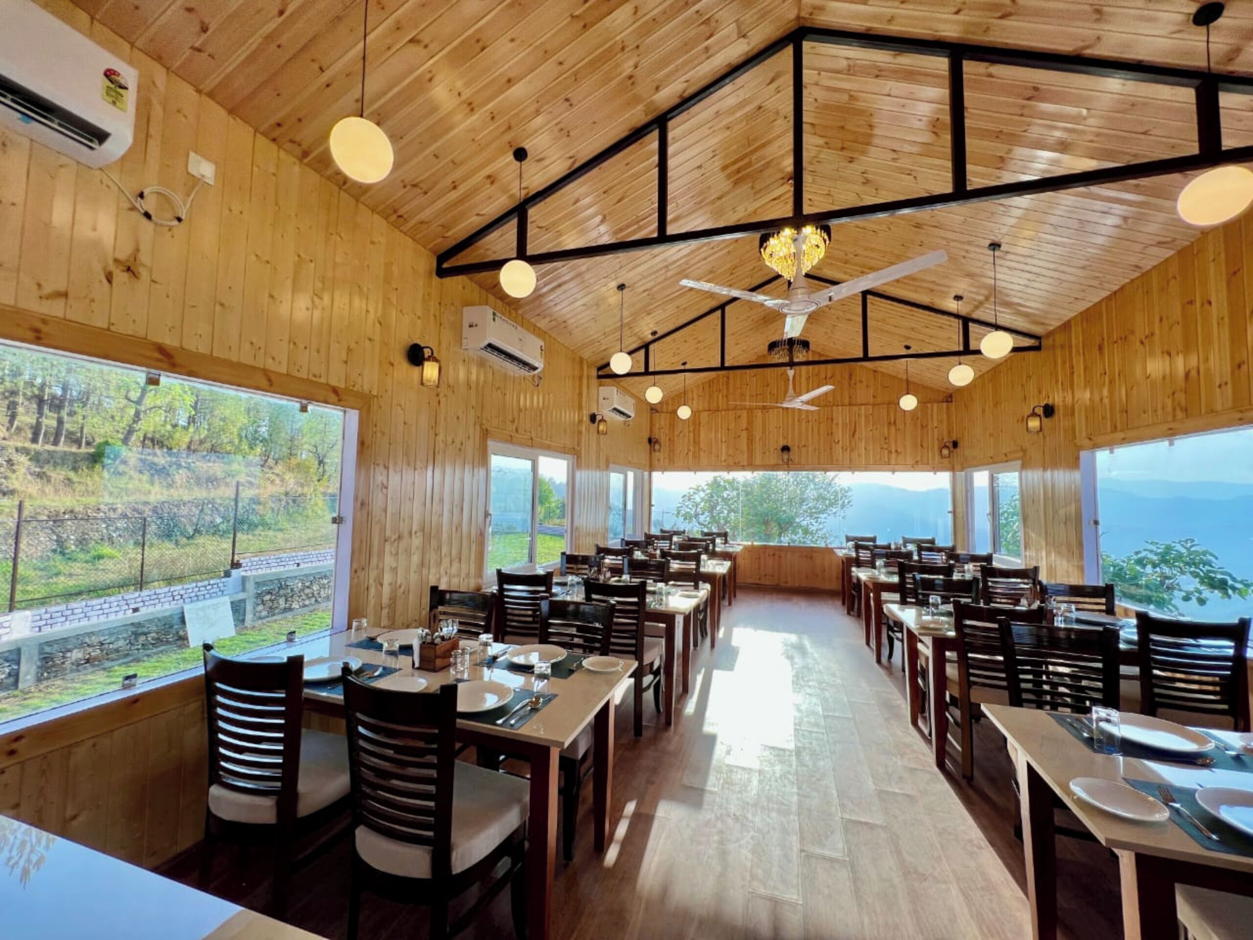 A restaurant with wooden walls and ceiling, large windows offering a view of the outdoors, and multiple dining tables and chairs.