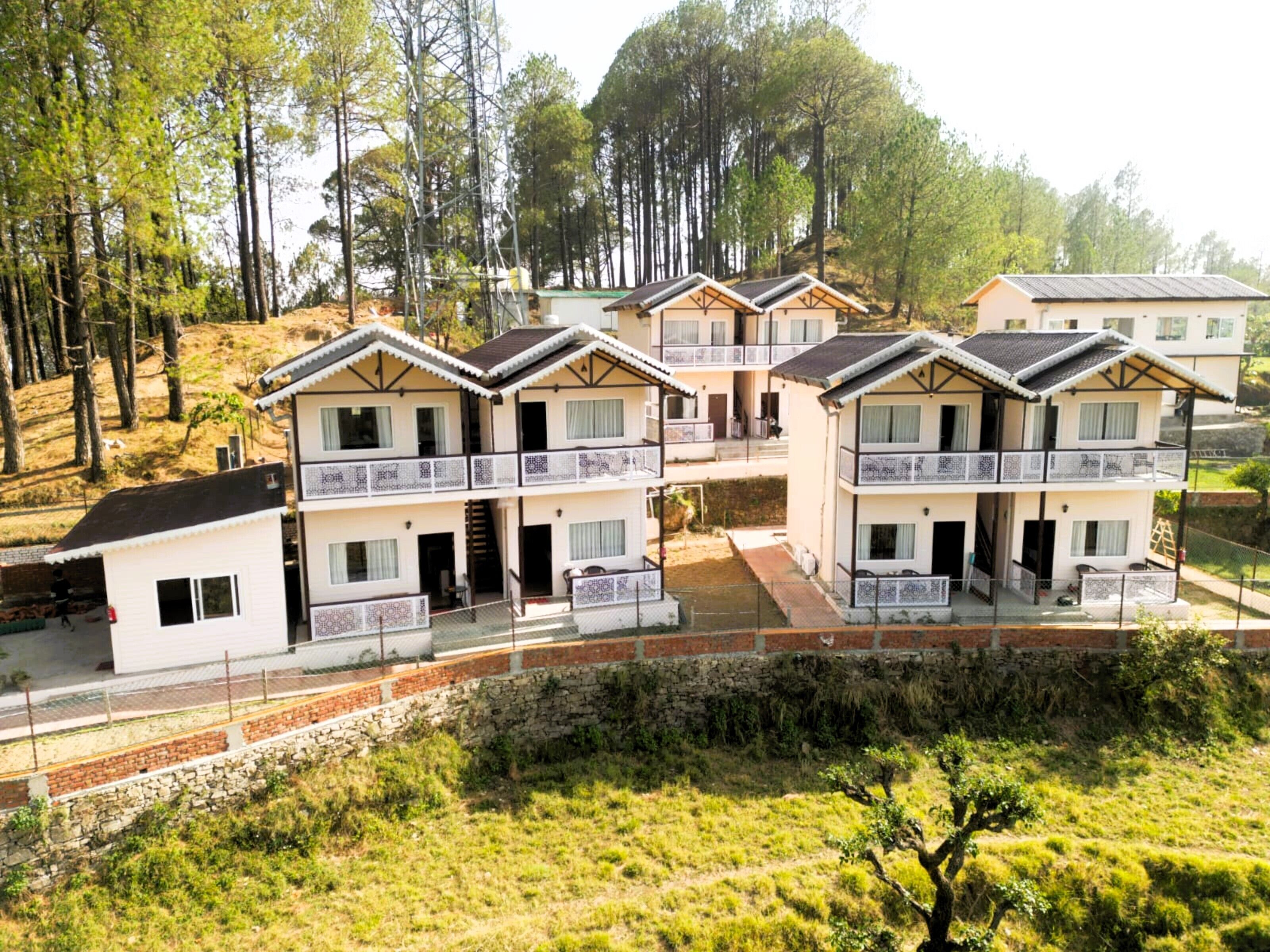 A row of two-story buildings with balconies, surrounded by trees and a stone wall.
