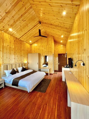 A wooden cabin bedroom with a bed, bedside tables, a desk, and a ceiling fan. - Hilltop Haven Hotel And Resort (Kotdwara)