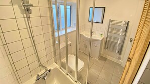 Egy modern fürőszoba üvegfalas zuhanyzóval, fürdőkáddal, WC-vel és egy mosdókagylóval, melynek felett tükör található.