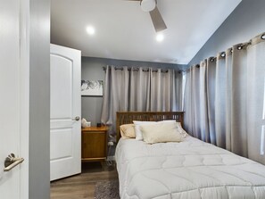 A bedroom with a bed, a nightstand, a ceiling fan, and curtains.