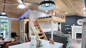 Un interior acogedor con comedor, una escalera que lleva a un altillo, chimenea y cocina moderna.