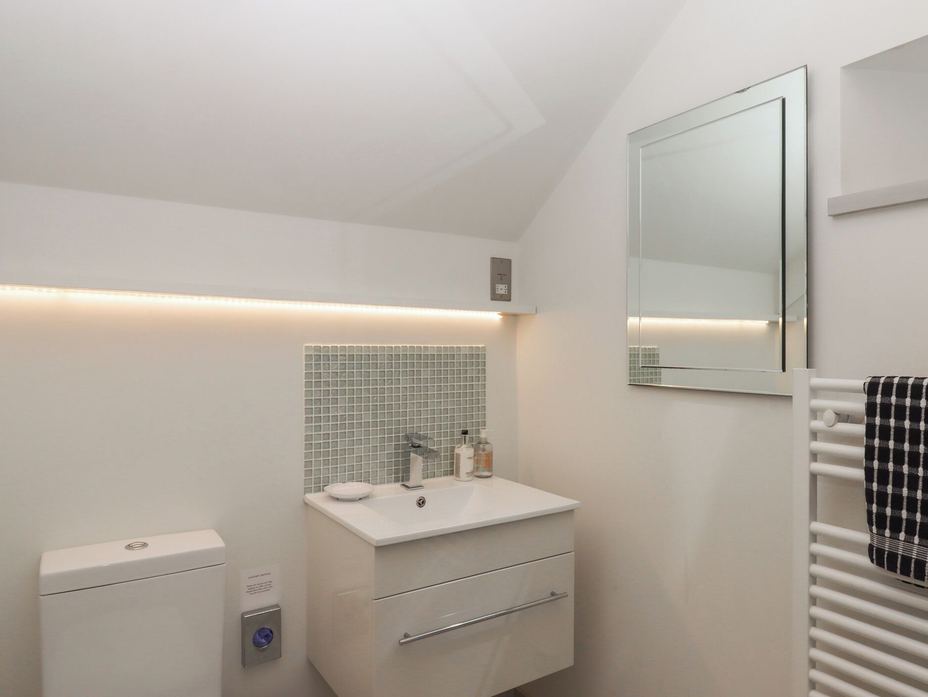 Un baño moderno con lavamanos blanco, espejo y toallero.