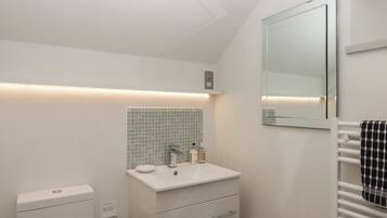 Un baño moderno con lavamanos blanco, espejo y toallero.