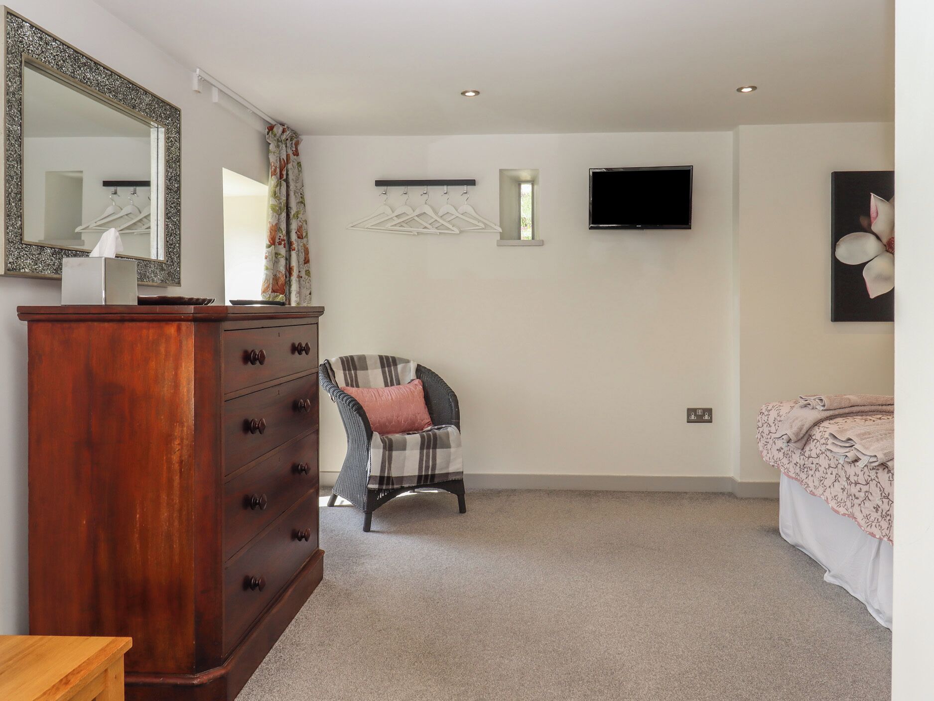 A bedroom with a wooden dresser, a chair, a bed, a TV, and a mirror.