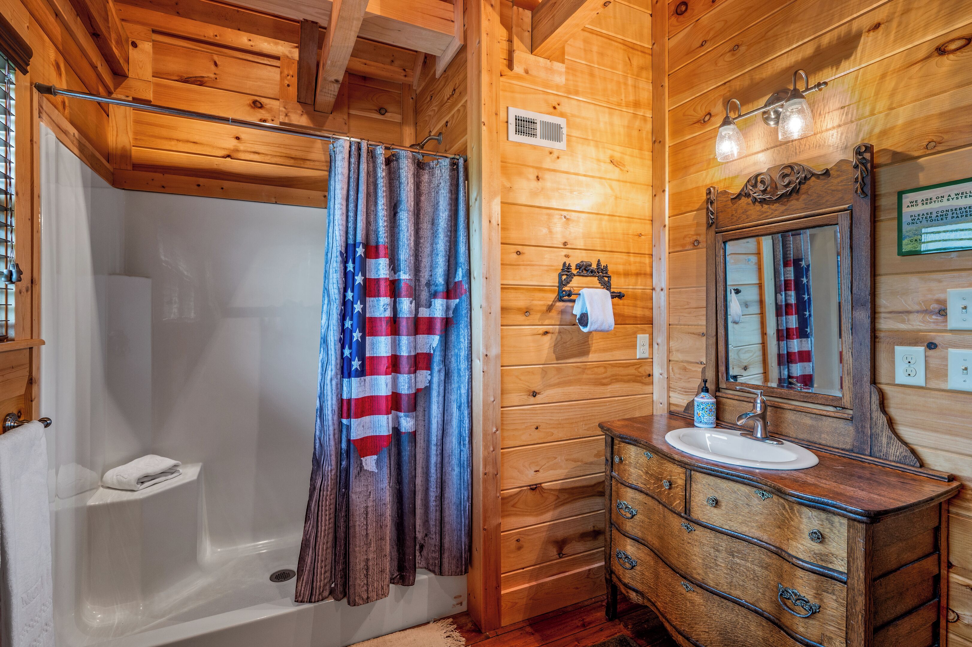 A wooden cabin bathroom with a shower, a sink with a mirror, and a towel rack.
