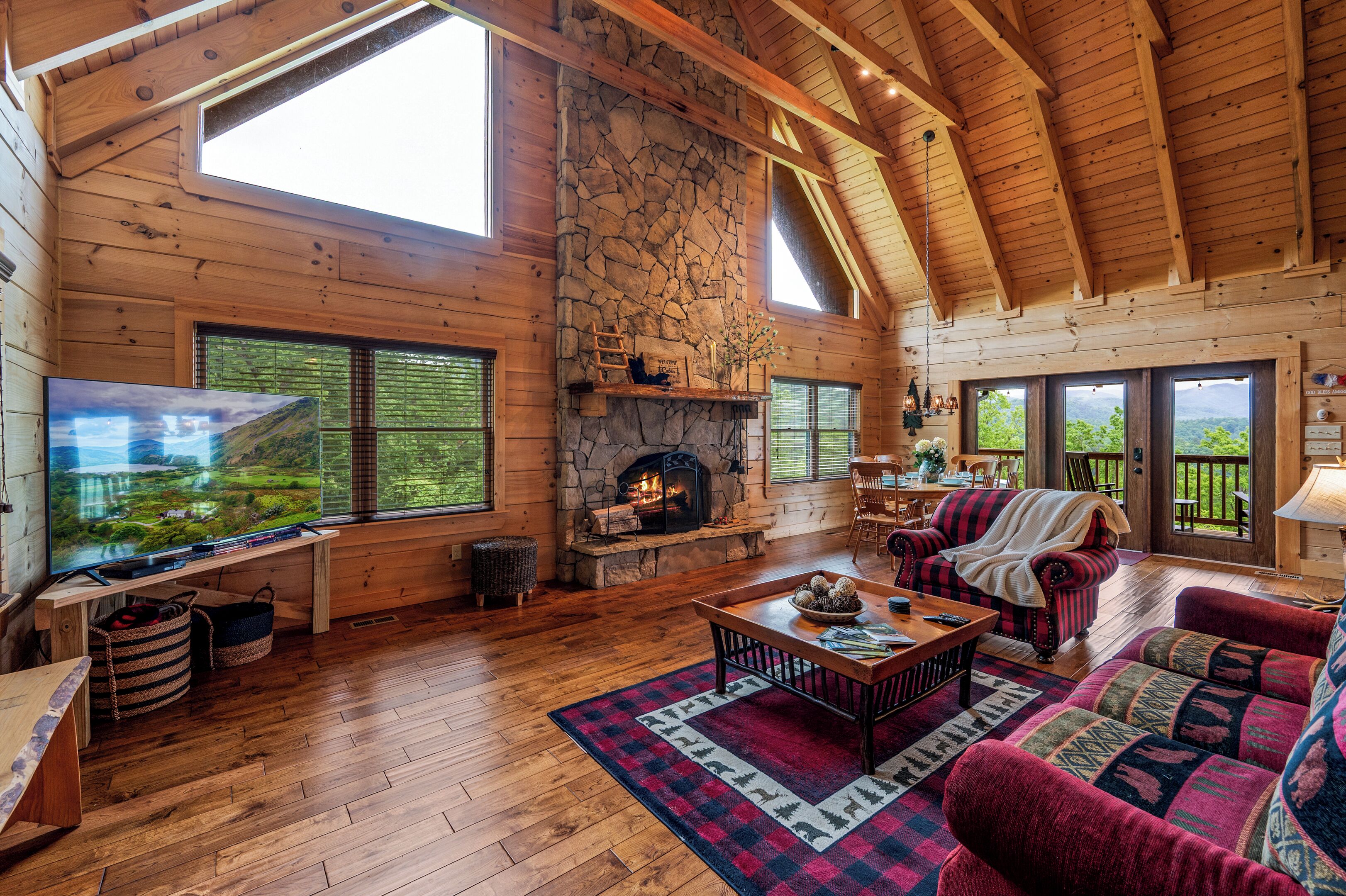 A spacious living room with a stone fireplace, wooden beams, large windows, and a cozy seating area.