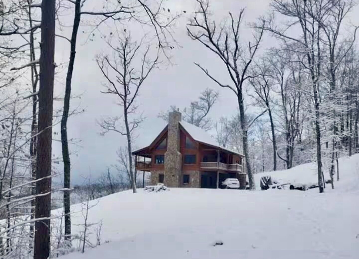 A rustic cabin with a stone chimney, surrounded by snow-covered trees.