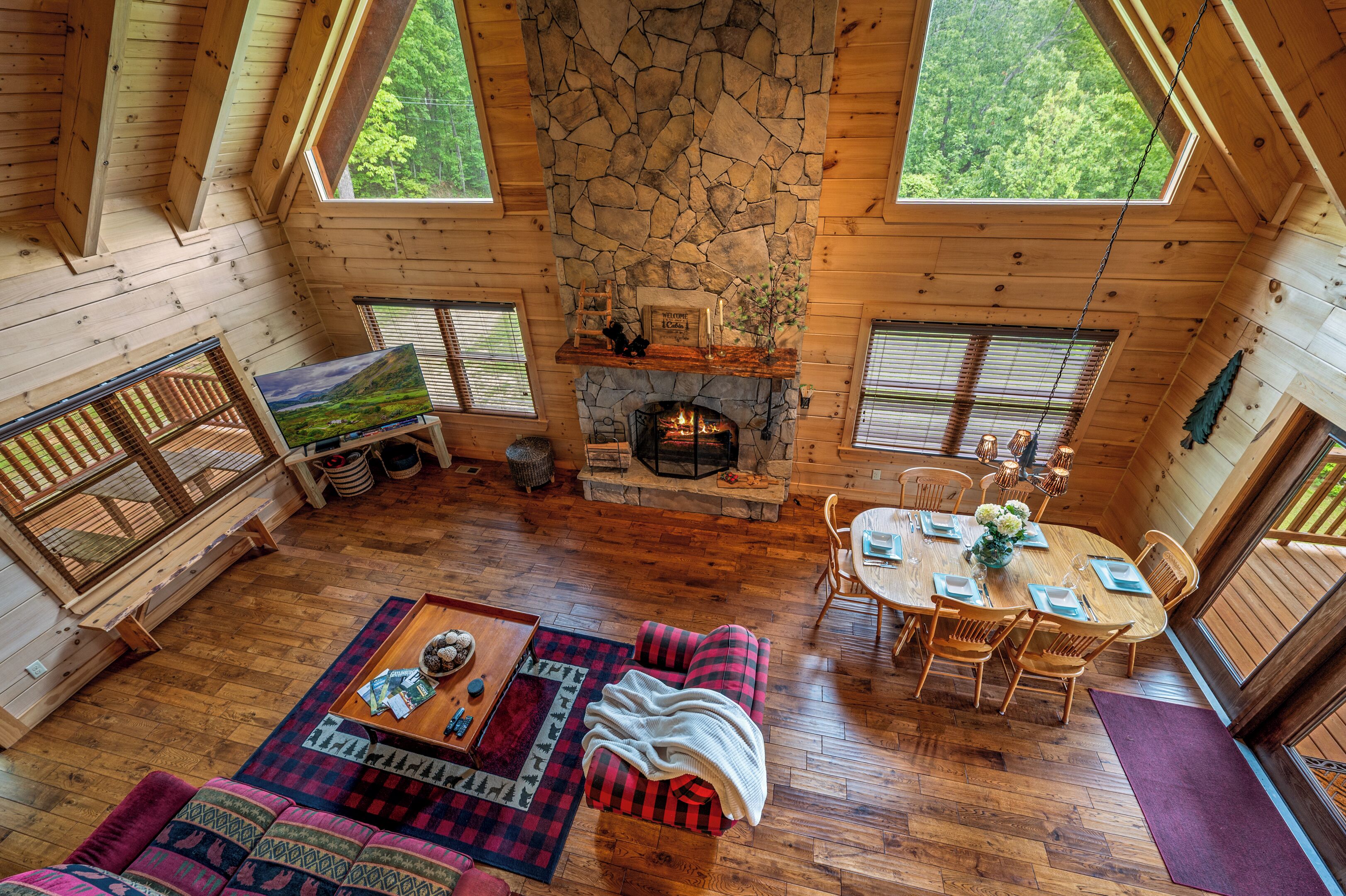 Interior acogedor de una cabaña con chimenea de piedra, pisos de madera, zona de comedor y un amplio ventanal con vistas a la vegetación.