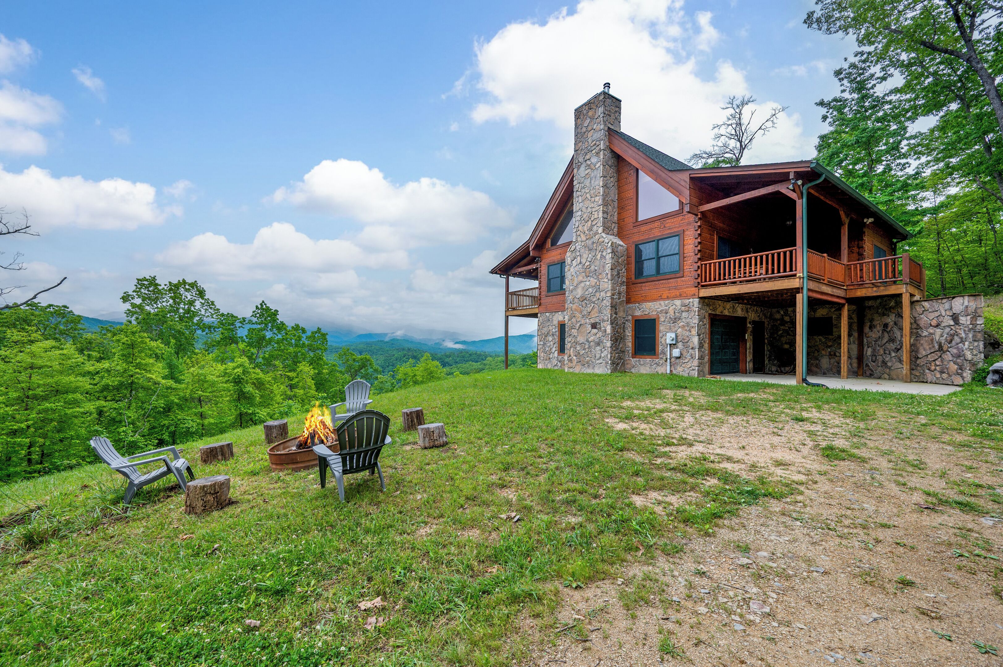 A stone cabin with a balcony, surrounded by a grassy area with outdoor seating and a fire pit.