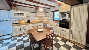 Uma cozinha com piso xadrez, armários de madeira, uma mesa de jantar com cadeiras, um lustre pendente e eletrodomésticos embutidos, incluindo micro-ondas e forno.