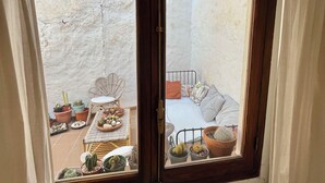Quarto com janela para uma varanda. A varanda tem uma cama, uma cadeira e diversos vasos de plantas.