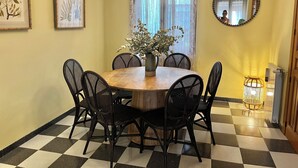 Uma sala de jantar com uma mesa redonda, seis cadeiras, um vaso com flores, um candelabro e um espelho na parede.