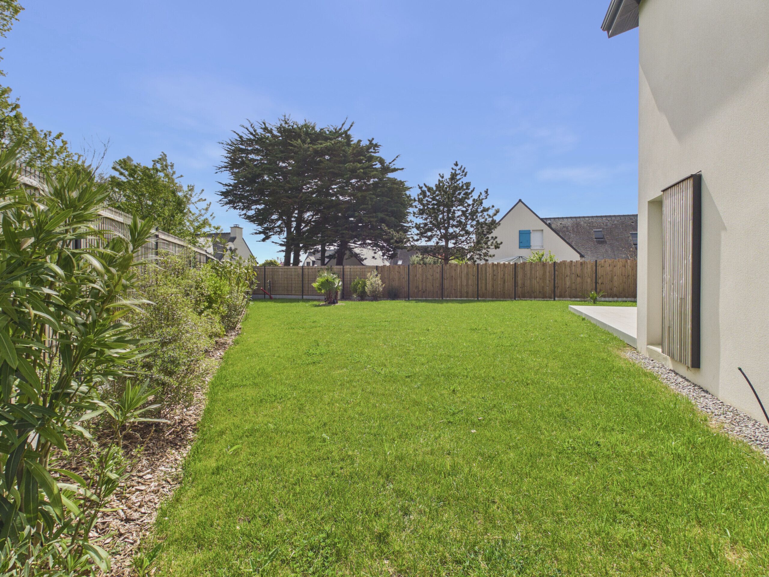 A well-maintained grassy yard with a wooden fence, a large tree, and a building with a window and door.