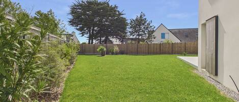 A well-maintained grassy yard with a wooden fence, a large tree, and a building with a window and door.