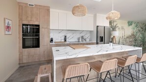 A modern kitchen with a marble island, wooden cabinets, and wicker bar stools.