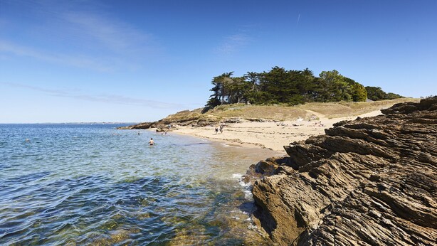 A coastal beach with rocky cliffs, clear blue water, and a sandy shore.